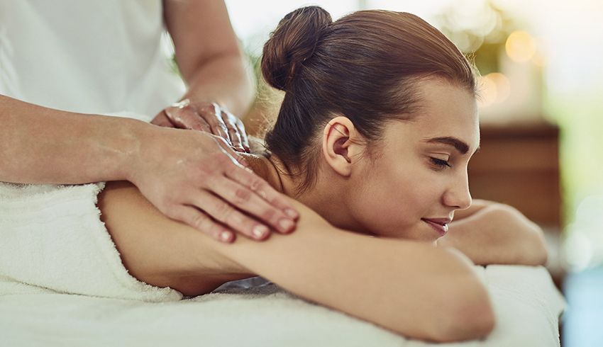 a woman lying on her stomach on a massage bed receiving a spa body treatment